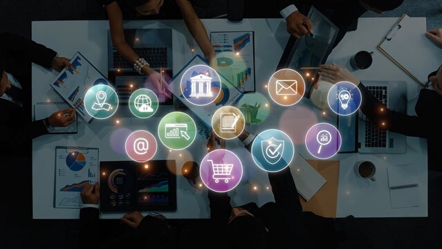Aerial view of a business team collaborating on a marketing strategy, featuring digital icons representing finance, communication, and data analysis in a modern workspace. Raster - Powered by Adobe