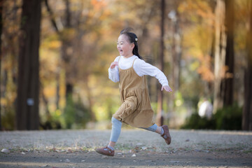 秋の紅葉の公園を元気に走る女の子の笑顔・無邪気さを捉えた明るい子どもの横顔