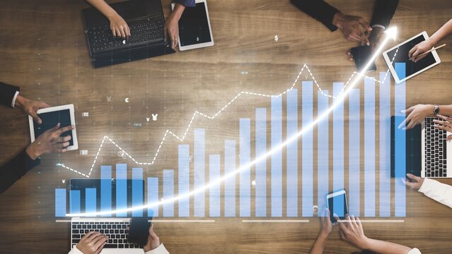 A diverse business team collaborates on data analysis using laptops and tablets, showcasing trends and growth in a modern workspace with a wooden surface. Copula