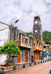 Municipal Palace or City Hall stands in Banos de Agua Santa, Ecuador. Historic stone building features tall clock tower and orange balconies near the central park