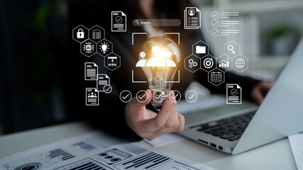 A business professional holds a glowing light bulb, surrounded by icons representing data and analytics, signifying innovative ideas and strategic planning in a modern office environment. Gantry