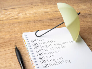 Checklist of various insurance categories on a notebook with a small umbrella. Protection,...