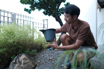 A man is kneeling down and holding a plant in a pot