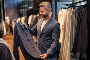 Trendy store with suit shirt. Business man choose suit for formal event. Trendy customer choosing jacket while shopping formal suit. Classic outfit. Shop manager show elegant suit. Perfect shirt