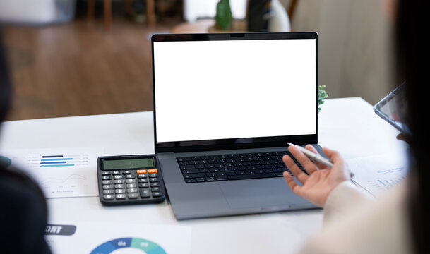 Close-up of a person's hand holding a pen, pointing toward the blank screen of an open laptop