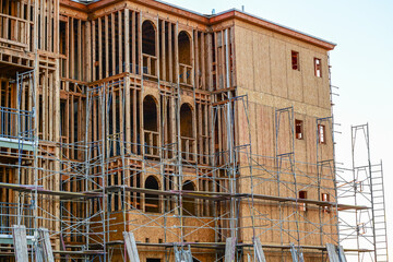 A multifamily residential building under construction with exposed wood framing, arched openings, and partial scaffolding, illustrating structural assembly and large scale housing development.