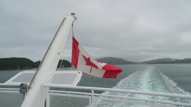 View from the back of a boat with Canadian flag, cloudy weather, and boat wake on windy sea.