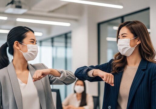 Two asian businesswomen in face masks elbow bump greeting in modern office - Powered by Adobe