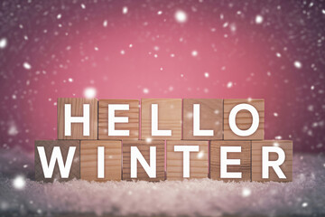 Wooden blocks spelling hello winter with falling snow against a pink background creating a festive seasonal atmosphere.