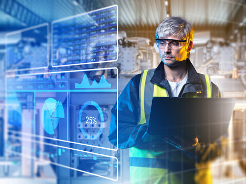 Industrial process engineer monitors production metrics on a laptop, analyzing performance dashboards and optimizing automated manufacturing operations for improved efficiency.
