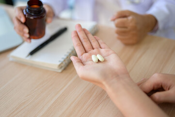 Close up of drug pill on patient's palm and doctor holding medicine bottle at diagnosis room's table
