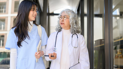 Young asian woman doctor talking to elderly senior while walking or standing in a clinic or hospital
