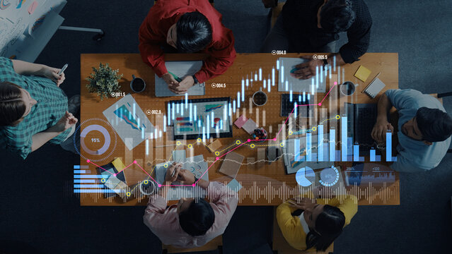 Aerial view of a business meeting showing diverse professionals discussing market trends using technology, charts, and data analysis for informed decision-making. Scalp - Powered by Adobe