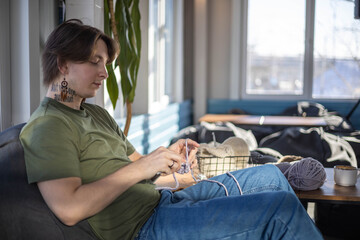 Hipster creative man crochet handmade use knitting supplies hook and wool yarn on couch at home