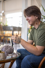 Hipster creative man crochet handmade use knitting supplies hook and wool yarn on couch at home