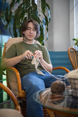 Feminine hipster man crochet handmade use hook knitting needles and wool yarn relaxing on couch