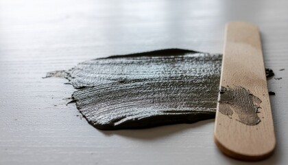 Thick dark green mud mask spread on a white surface with wooden applicator
