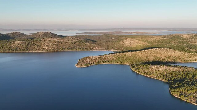 Drone turns over Telascica bay, revealing Dugi Otok&rsquo;s hilly terrain, lush forests, and scattered islands in sunset light.