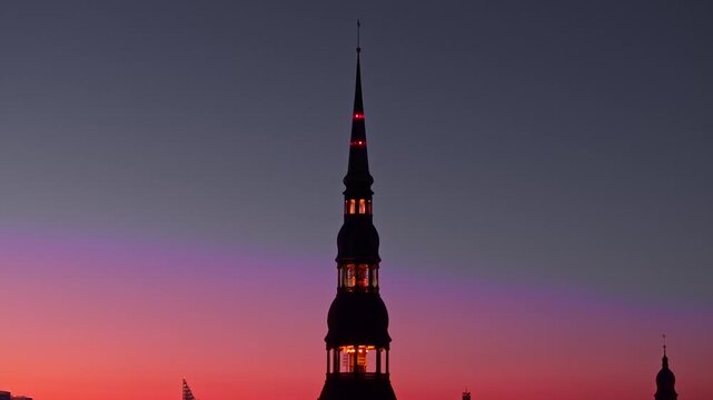 Slow drone orbit of St Peter&rsquo;s Church tower with warm sunset hues over Riga city
