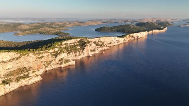 Drone glides along Telascica cliffs on Dugi Otok, revealing Kornati islands in golden sunset light over the Adriatic.