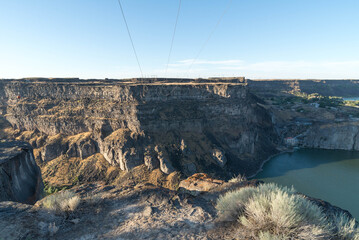 View from below power lines spanning the massive Snake River Canyon, with scrub brush dotting the flat plains and colored by harsh shadows. 