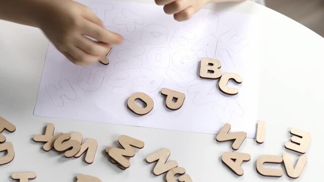 A small preschool boy diligently assembles a wooden puzzle with the English alphabet. The child studies the letters.