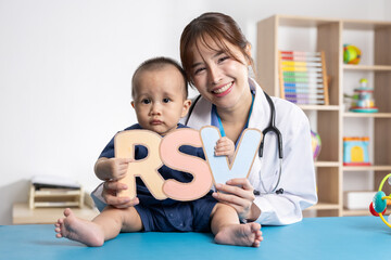 Asian pediatric doctor smiling while holding RSV letters with infant, promoting awareness of respiratory infections and child health in bright clinical. Suitable for healthcare and education