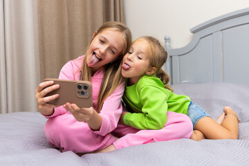 Two sisters taking a selfie and making funny faces on a bed at home