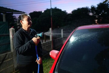 The woman in the black shirt is intentionally spraying water onto the side of the red car.