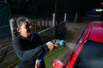 A close-up shot of a woman holding a nozzle and hose to spray water on the red car.