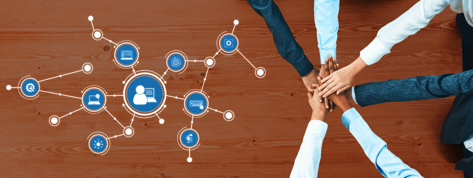 A diverse group of professionals joining hands on a wooden desk with digital icons, showcasing collaboration and technological innovation in a modern workspace. Amity - Powered by Adobe