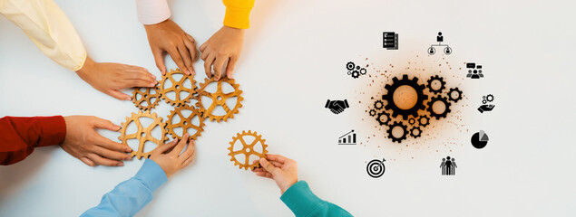 Diverse hands work collaboratively to arrange gears on a table, symbolizing teamwork and business...