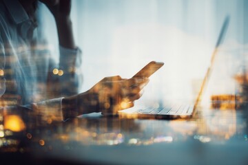 Businesswoman engaged in communication using smartphone while working on a laptop in a modern office environment during evening hours