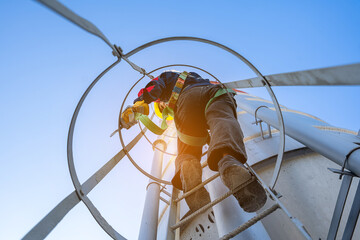 A worker or engineer, wearing essential safety equipment including a harness and a yellow hard hat, is captured climbing a fixed vertical ladder on the side of a large industrial silo.