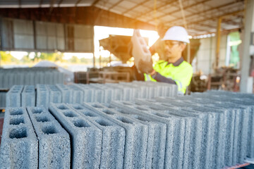 A construction workers wearing protective clothing carefully inspect stacking hollow concrete blocks (concrete blocks) in an indoor factory or construction material storage area.