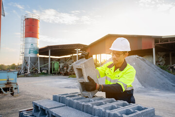 Asian male engineer wearing protective clothing inspecting concrete blocks (cinder blocks) outdoors, wide angle shot.