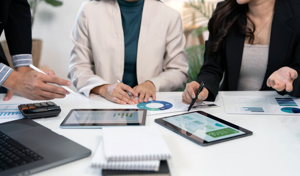 Business professionals collaborate, analyze financial data, and discuss marketing strategy using digital tablets and documents in a modern office meeting.