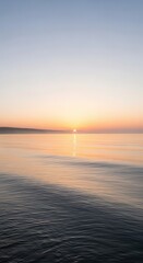 Fototapeta premium Distant sun reflects upon calm water surface during soft twilight