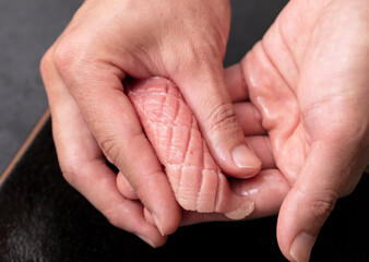 A sushi chef places a piece of raw yellowtail fish in his hands while making sashimi. 