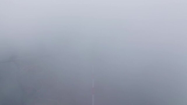 Static aerial drone shot of Riga TV tower emerging from a low cloud bank