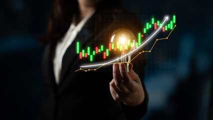 A business professional stands confidently holding a light bulb, symbolizing innovative ideas, with a digital stock market chart illustrating financial trends and growth. Impute