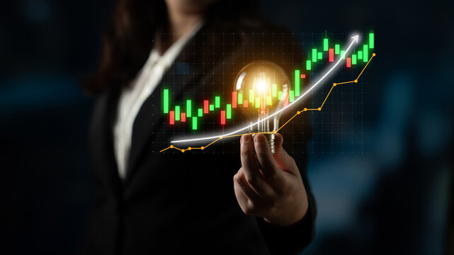 A business professional stands confidently holding a light bulb, symbolizing innovative ideas, with a digital stock market chart illustrating financial trends and growth. Impute