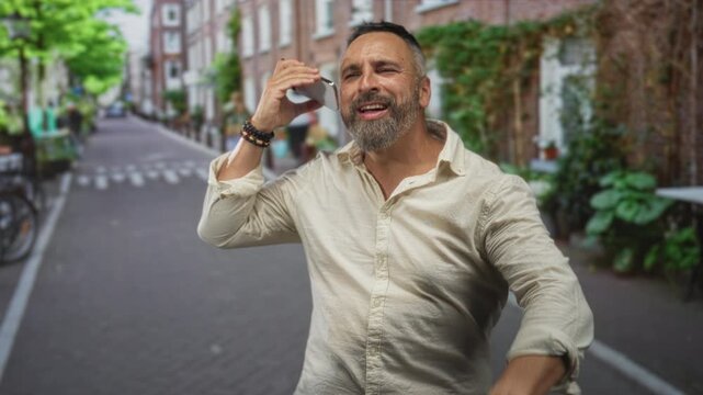 Man holding phone to ear, smiling and dancing on a narrow city street while bracelets show on his wrist; joy celebration.
