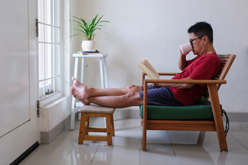 man sitting alone on armchair reading a book at weekend