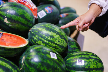 Customer selecting fresh watermelon in supermarket, hand pointing at ripe fruit, healthy shopping and fresh produce concept.
