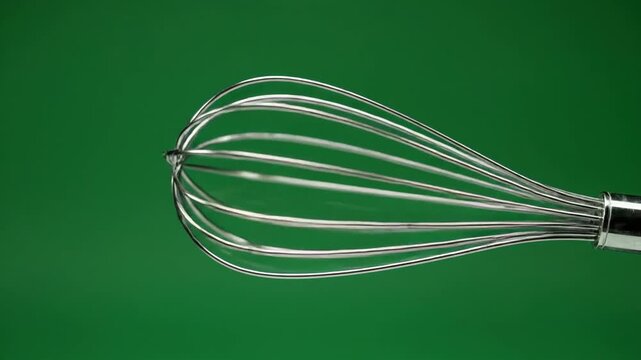 Close-up of a metal whisk against a solid green background, with a white border at the bottom, showcasing floating household objects on an isolated green screen.