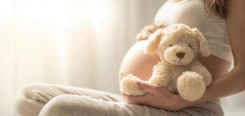 The pregnant woman cradling a teddy bear and her baby bump in soft light
