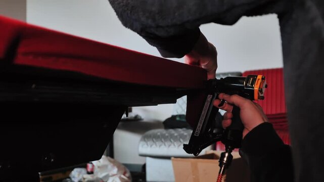 Close up of craftsman stapling vivid red fabric under billiard table, Latvia