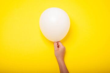 The child is holding a white balloon on a white background. Unrecognizable child. Birthday concept.