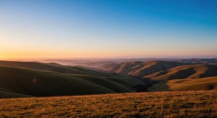 Fototapeta premium Sunrise over rolling hills. Vast landscape bathed in golden light. Soft, hazy atmosphere. Distant valleys